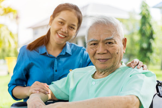 Portrait of Young Asian caregiver in uniform hugging smiling elderly man or patient in wheelchair during a home visit and spending time together. Love, Family or Assistant or elderly caregiver concept