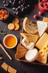 Fototapeta premium Various types of cheese in wooden box, honey, nuts, crackers, grapes