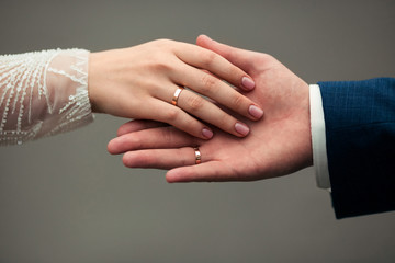 Close-up caressing hands of newlyweds. Gentle touch of hands of loving couple of newlyweds. Beautiful and romantic holding hands with woman`s hand on top of man`s hand with wedding rings on close up