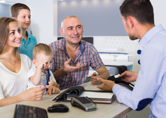 Fototapeta premium Young smiling family choosing material for mattress with salesman in salon