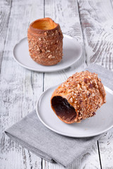 Trdelnik covered in nuts and sugar with chocolate inside against white wooden background. Czech street food