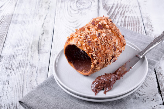 Trdelnik covered in nuts and sugar with chocolate inside against white wooden background. Czech street food