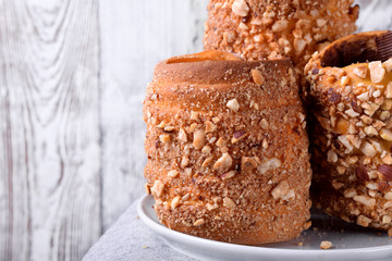 Trdelnik covered in nuts and sugar with chocolate inside against white wooden background. Czech street food