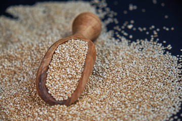 White quinoa seeds on a black background. quinoa in spoon on kitchen table top view. Healthy and diet superfood product.