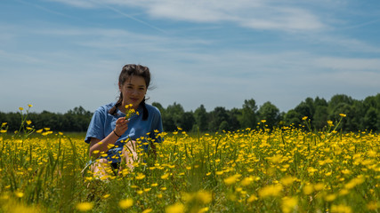 Teen girl sitting in large field with yellow flowers and trees in the background