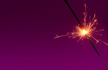 Burning christmas sparkler on purple background with room for text