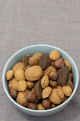 Mixed nuts, including almonds, hazelnuts, walnuts and Brazil nuts, in shells in a bowl.  Grey cloth background