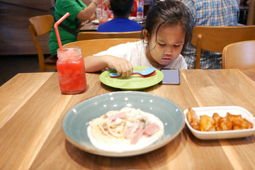 An Asian girl plays a smart phone on the dining table.