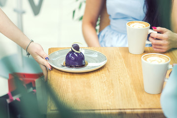 The female hand is putting the piece of cake on the table in cafe. Waiter puts the dessert on the table at cafe.