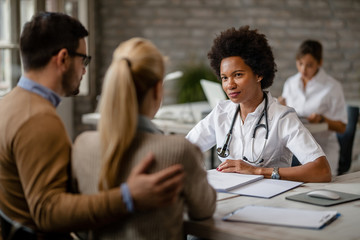 African American doctor talking to a couple at clinic.