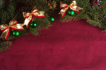 Branches of spruce decorated with balls with bows on a burgundy background. Christmas background. Copy space.
