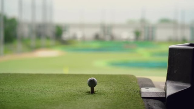 Close-up of golf ball on tee with golf club overlooking driving range at Topgolf