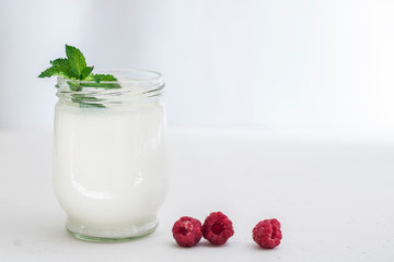 Organic probiotic milk kefir drink or yogurt in glass containers, with raspberry, on the white grey...