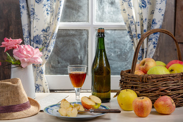 Bottle and glass of cider with apples. In rustic house