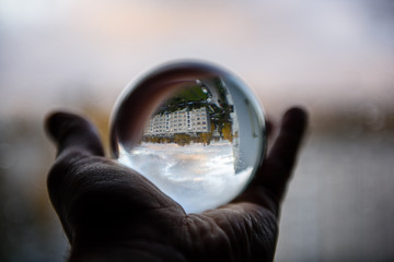 male hand holding crystal glass ball against nature background with reflections