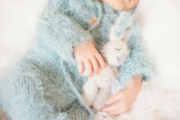 Newborn Baby. Sleeping Baby In Bed, Holding A Bunny Toy. Baby With Blue Knitted Romper