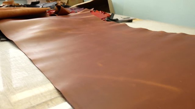 A skinner unfolds a roll of leather on a table. Leather master choosing twisted piece of leather. Close up 4k