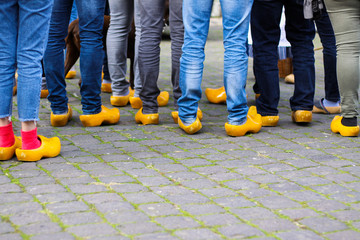 Close up of blue jeans legs of group of people wearing traditional wooden clogs during guided city...
