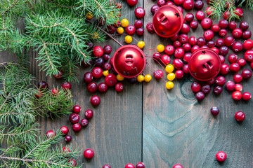 Green branches of the tree, bright cranberries and red bells on a wooden background.