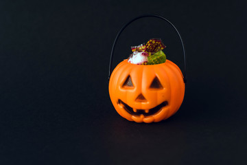 Orange plastic candy basket in the shape of a pumpkin jackolantern on a black background