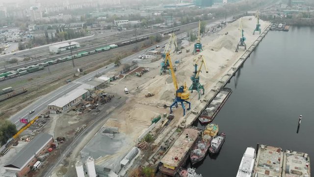 Aerial view of port working cranes extracting sand from iron barge and scow on river bank in industrial dirty city in smog