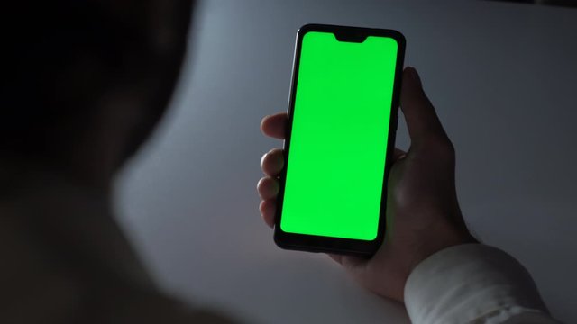 Man using a Smartphone with Green Mock-up Screen in office at night