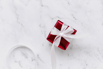 Gift in red shiny paper with a pink long ribbon on a marble background top view.