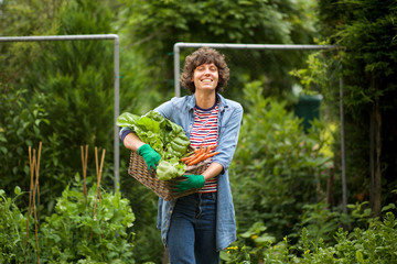 female farmer smiling with bunch of vegetables in basket by farm