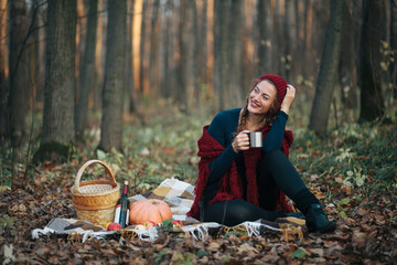 Beautiful girl in a red hat on a picnic in the autumn forest