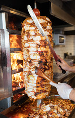 Chef cutting with doner knife Traditional Turkish Doner Kebab meat. Shawarma or gyros. Turkish, greek or middle eastern arab style chicken doner kebab food on isolated white. - obrazy, fototapety, plakaty