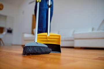 Young cleaner sweep the floor in living room. Cleaning service