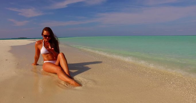 Attractive young brunette woman sunbathing on the white sand beach and looking on the different stones and seashells that waves brings to her