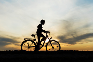 Obraz premium Boy , kid 10 years old riding bike in countryside, silhouette of riding person at sunset in nature