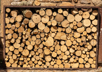 Stacks of cut logs and branches for firewood in frame by stone wall of old house