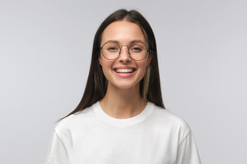 European girl wearing big round glasses smiling happily at camera, isolated on gray background