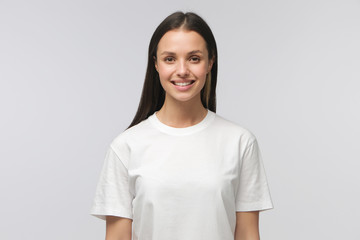 Closeup of young European lady standing in front of camera in white T-shirt with calm happy smile,...