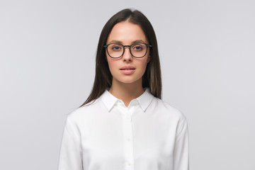 Portrait of European girl wearing glasses and formal shirt for office work, isolated on grey background