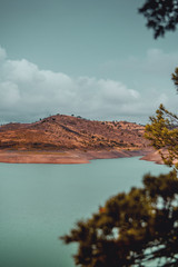 Countryside mountain landscape view with turquoise dam lake on a dark and moody rainy day with clouds. Serra de Monchique, Algarve in Portugal