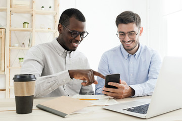 Two colleagues, African and Caucasian guys, working together sharing information on smartphone