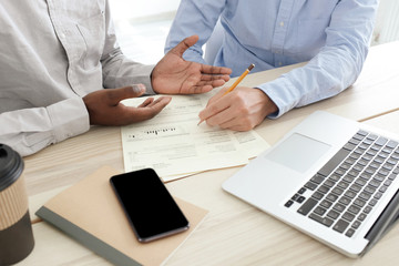 Photo of hands of two men analysing data and writing on papers on desk in office
