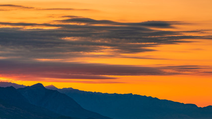 Fototapeta na wymiar Sunset with the layered mountains, orange sky and clouds