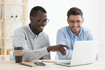 African guy pointing to data on laptop for his European colleague while working together on...