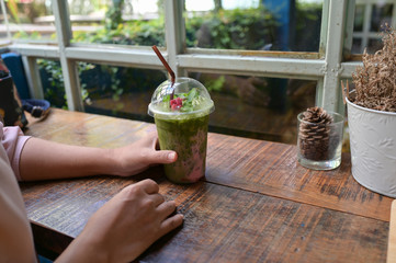 Woman with glass of matcha green tea with ice in hand sitting at wood table in coffee shop