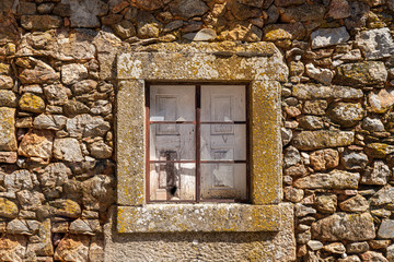 Broken glass pane and wooden shutters in stone window and wall of old house in the ancient town of Castelo Rodrigo in Portugal