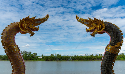 Two serpent or nagas statues are spraying water, with the sky and river as the background.