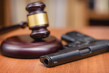 Court illegal use of weapons. Sentence for murder. Judge's gavel on wooden table. Judge, hammer, pistol on wooden background.Selective focus.