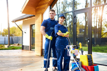 Fototapeta premium Two friends from cleaning service busy with house cleaning session, stand closely outdoors, cleaning cottage, country house. Hygiene concept.