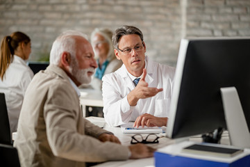 Doctor and his senior patient analyzing medical reports on a computer at clinic.