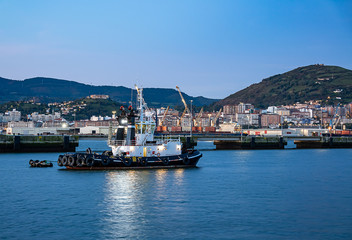 Fototapeta na wymiar Tugboat with cranes and houses in the background