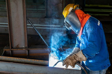 The welder is welding a steel structure with the process Flux Cored Arc Welding (FCAW) in Industrial factory.
